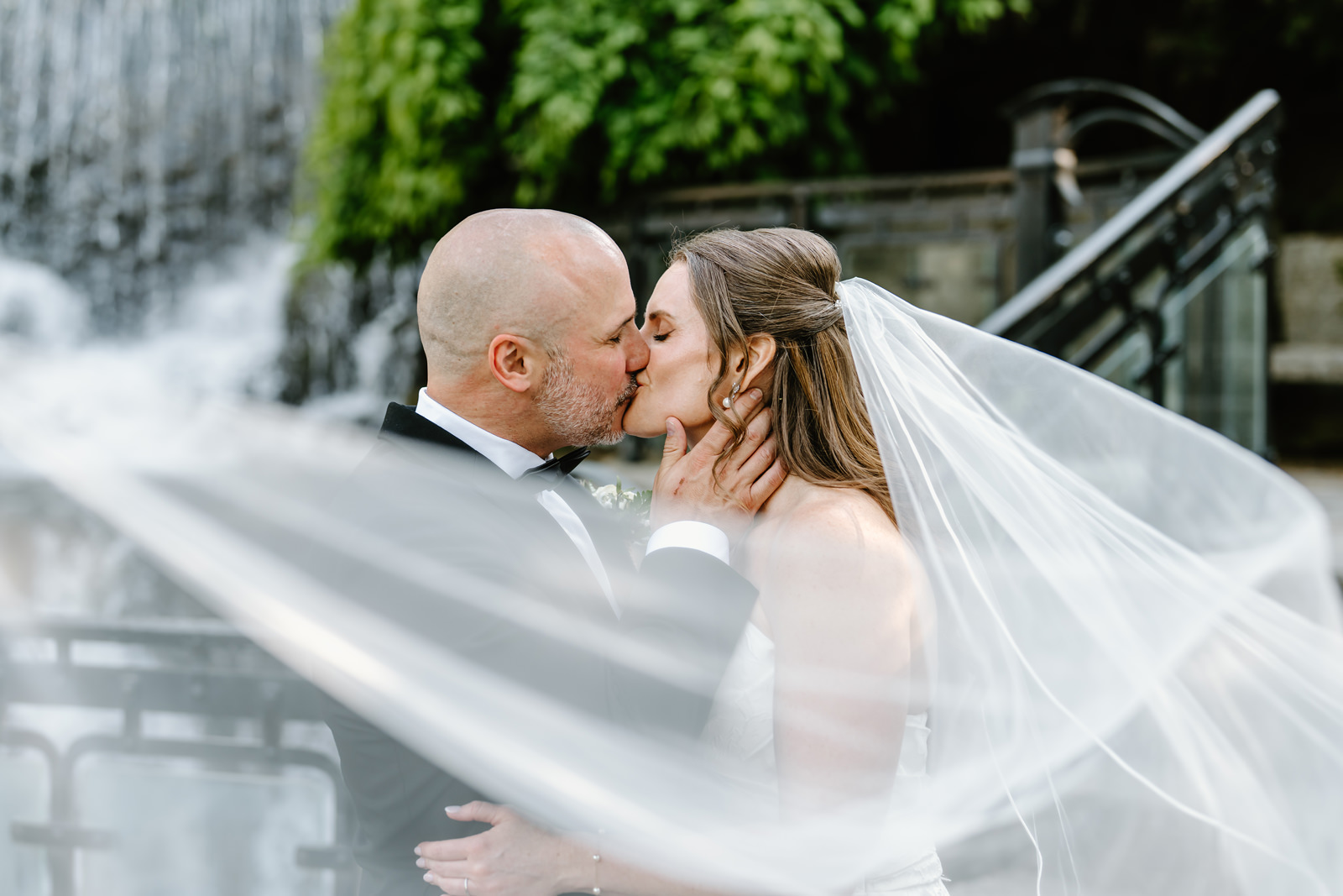 Newlyweds kissing in front of the waterfall at Ancaster Mill
