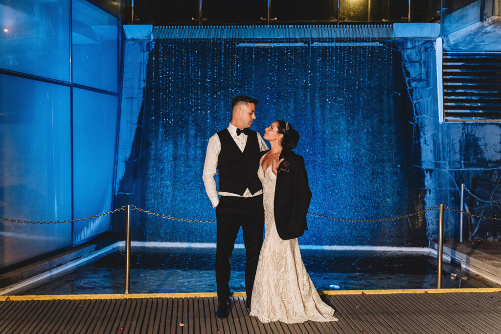 A night shot of newlyweds in front of the Waterfall at Spencer's at the Waterfront